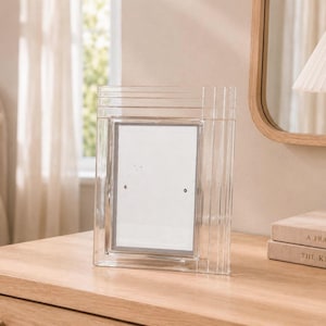 May include: A rectangular picture frame made of clear, thick glass with a stepped, layered border design. The frame features a central vertical opening for a photograph and has a smooth, transparent finish that reflects light across its surface.