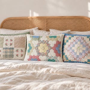 May include: Three rectangular quilted pillows arranged on a bed. The left pillow features a grid of floral and plaid squares. The center pillow displays a hexagonal patchwork pattern in pastel tones. The right pillow has a blue border and a central diamond motif.