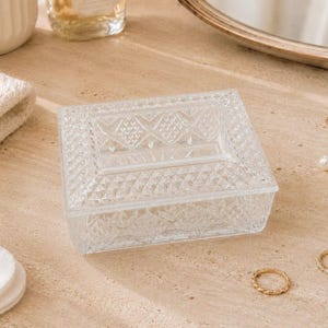 May include: A rectangular clear glass trinket box featuring a pressed diamond pattern on the lid and sides. The box has a flat, smooth top panel surrounded by a textured geometric border, providing a transparent storage container for small items.