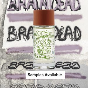 May include: A clear glass perfume bottle with a brown cylindrical cap. The bottle features green line art illustrations of hands, flowers, and stars, with the text "TERRA" and "PERFUME" printed on the front. The label also displays "50ml / 1.7 FL OZ."