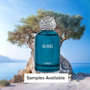 May include: A teal-colored perfume bottle with the word "DELPHES" in white lettering. The bottle has a textured, white cap. The words "L'OBJET" are below the name. The background features a tree, ocean, and sky. The text "Samples Available" is at the bottom.