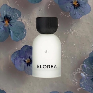 May include: A white cylindrical perfume bottle with a black cap, featuring the text GIT and ELOREA in black lettering. The bottle is surrounded by several blue pansy flowers with yellow centers, submerged in clear liquid with visible air bubbles.