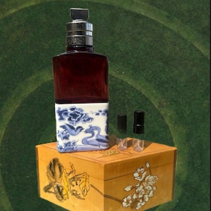 May include: A dark red glass bottle with a silver cap and a white and blue patterned base, featuring birds and swans. The bottle sits on a wooden box with floral designs. Two black caps and three clear stoppers are also present.