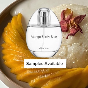 May include: An oval-shaped perfume bottle labeled "Mango Sticky Rice" sits on a plate with mango slices and sticky rice. The bottle is clear with a silver sprayer. The plate has a brown rim and the text "Samples Available".