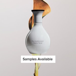 May include: A white perfume bottle with a black cap and the text "The Harmonist Matrix Metal." The bottle is set against a backdrop of a golden-brown leaf. The text "Samples Available" is displayed below the bottle.