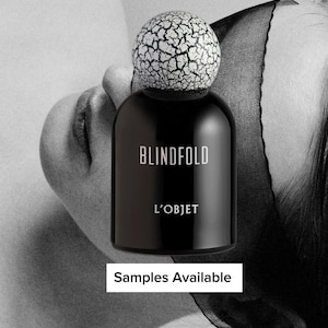 May include: A black perfume bottle with a cracked white cap. The bottle has the word "BLINDFOLD" and "L'OBJET" printed on it. The image also includes the text "Samples Available".