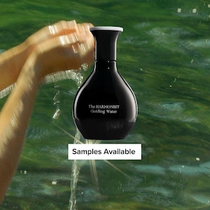 May include: A black perfume bottle with a white cap, featuring the text "The HARMONIST Guiding Water." The bottle is set against a green water background. The words "Samples Available" are also visible.