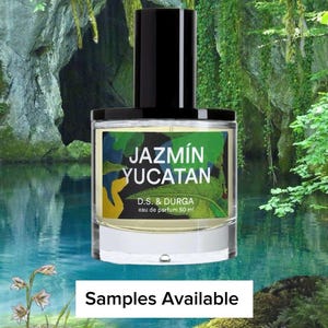 May include: A clear glass perfume bottle with a black cap, labeled "Jazmín Yucatan." The label features green, blue, and yellow abstract art. The bottle is set against a backdrop of a serene lake and lush greenery. The text "Samples Available" is at the bottom.