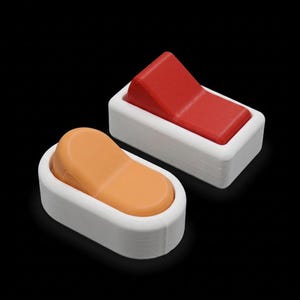 May include: Two plastic light switches with white rectangular bases. One switch features a red, angled, rectangular toggle, while the other features an orange, rounded, oval-shaped toggle. Both switches have a smooth, matte finish.
