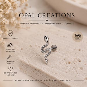 Pode incluir: Uma joia corporal em forma de serpente prateada com pedras claras e um suporte traseiro plano. O texto diz OPAL CREATIONS, 16G, 1.2MM, HYPOALLERGENIC, SOLID G23 TITANIUM, INTERNAL THREAD e COMFORTABLE FLAT BACK.