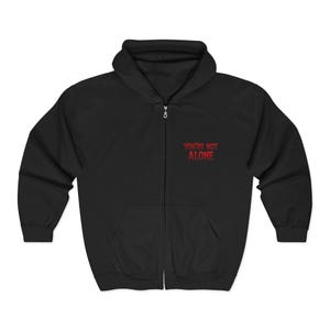 May include: Black zip-up hoodie with a hood and front pockets. The phrase "YOU'RE NOT ALONE" is printed in red on the upper left chest area. The hoodie has a silver zipper and a drawstring hood.