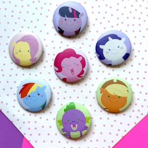 May include: A collection of seven round, colorful buttons featuring cartoon pony characters. Each button has a different character design with various colors, including purple, pink, blue, yellow, and green. The buttons are arranged on a polka dot background.