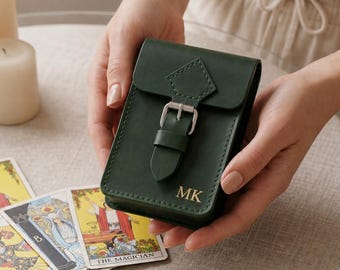 Könnte beinhalten: Eine dunkelgrüne Ledertasche mit Schnallenverschluss und den goldgeprägten Initialen MK auf der Vorderseite. Das rechteckige Etui verfügt über einen Klappdeckel mit rautenförmigem Detail und eine silberfarbene Metallschnalle für Tarotkarten.