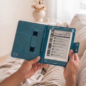 May include: Teal leather e-reader case with the initials "FB" embossed on the front. The case is open, revealing an Onyx Boox Darwin 5 e-reader and a matching teal stylus. The e-reader is held in place by a frame.