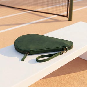 May include: A dark green, teardrop-shaped protective case for a pickleball paddle. The case features a smooth, matte finish, a wrap-around zipper closure with a matching pull tab, and a detachable wrist strap with a metal lobster clasp attachment.