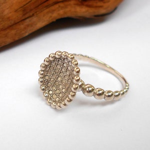 Könnte beinhalten: Ein silberner Ring mit einem strukturierten, runden, perligen Design. Der Ring besteht aus kleinen, runden Perlen, die zu einem einzigartigen und auffälligen Design zusammengefügt sind.