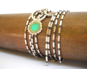 May include: A silver chain necklace with a green gemstone pendant. The pendant is surrounded by a silver and gold floral design.