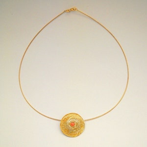 Puede incluir: Un collar de cadena de oro con un colgante redondo que presenta un delicado dise&ntilde;o de filigrana y una peque&ntilde;a piedra redonda de color coral en el centro.