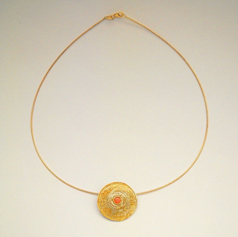 Puede incluir: Un collar de cadena de oro con un colgante redondo que presenta un delicado dise&ntilde;o de filigrana y una peque&ntilde;a piedra redonda de color coral en el centro.