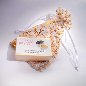 May include: A small white box with a gold and white patterned bag. The box has the text "www.welnerjewellery.com/gallery" and "Phone: 052-4487200" printed on it. The box contains two silver rings with a black and white design.