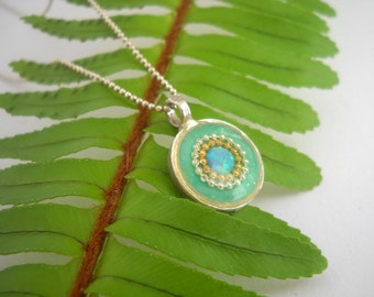 May include: A silver chain necklace with a round pendant featuring a turquoise blue resin background with a gold and silver beaded circle surrounding a light blue opal.