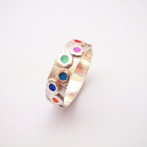 May include: A silver ring with a textured band and seven colorful enamel dots. The dots are red, orange, yellow, green, blue, indigo, and violet.