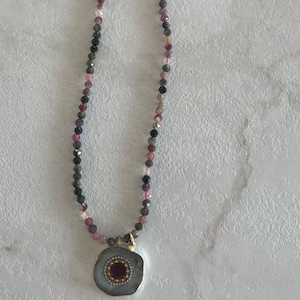Op de afbeelding: Een ketting met een veelkleurige kralenketting en een zilveren hanger met een roze edelsteen in het midden.