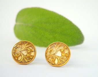 May include: A pair of gold-toned earrings with a delicate floral design. The earrings are round and have a clear resin center.
