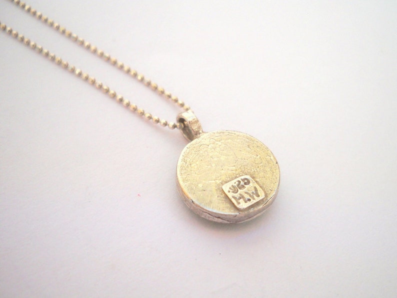 May include: Silver necklace with a round pendant. The pendant has a textured surface and the inscription "925 MW" on the back.