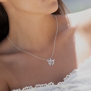 May include: A silver necklace with a delicate pendant featuring the Hebrew letter Chai, a symbol of life. The necklace is worn by a person with a white shirt.