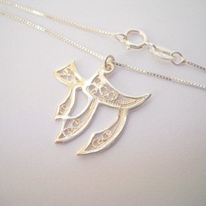 May include: A silver chain necklace with a delicate filigree pendant in the shape of the Hebrew letter Chai. The pendant is intricately designed with a floral pattern.