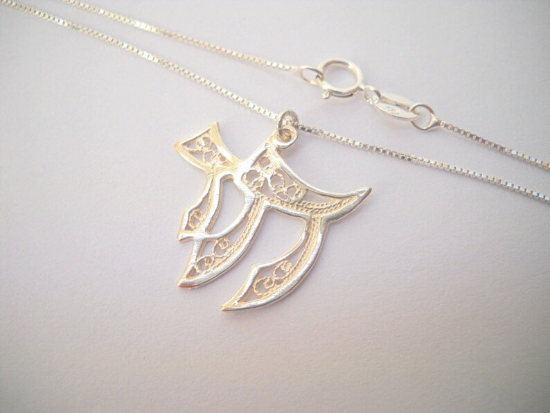 May include: A silver chain necklace with a delicate filigree pendant in the shape of the Hebrew letter Chai. The pendant is intricately designed with a floral pattern.