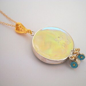 Puede incluir: Un collar de plata con un colgante redondo iridiscente, cadena de oro y abalorios de ojo azul. La parte posterior del colgante tiene la inscripci&oacute;n "925 Italy".