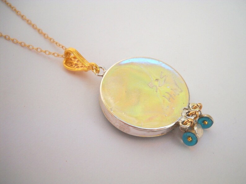 Puede incluir: Un collar de plata con un colgante redondo iridiscente, cadena de oro y abalorios de ojo azul. La parte posterior del colgante tiene la inscripci&oacute;n "925 Italy".
