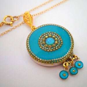 Puede incluir: Un collar de cadena dorada con un colgante turquesa que presenta un centro de &oacute;palo dorado y blanco. El colgante tiene un dise&ntilde;o de filigrana dorada y tres abalorios en forma de l&aacute;grima turquesa.