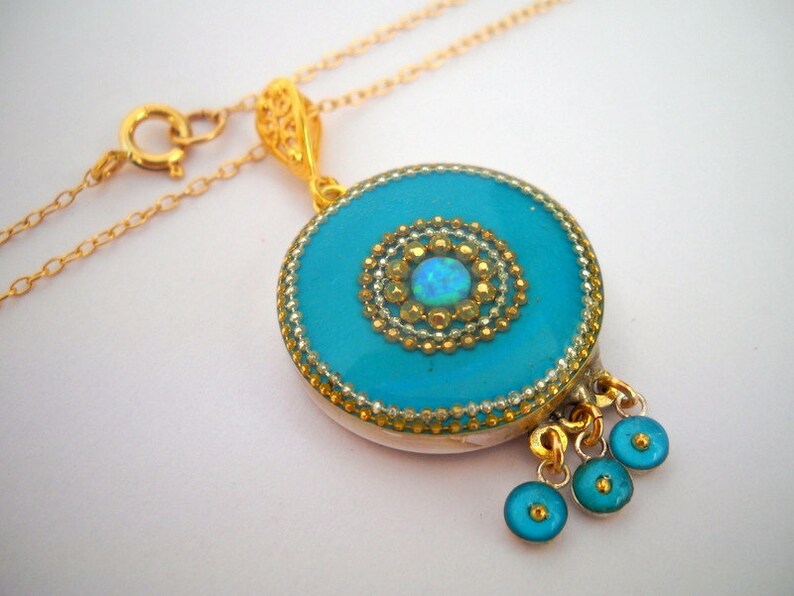 Puede incluir: Un collar de cadena dorada con un colgante turquesa que presenta un centro de &oacute;palo dorado y blanco. El colgante tiene un dise&ntilde;o de filigrana dorada y tres abalorios en forma de l&aacute;grima turquesa.