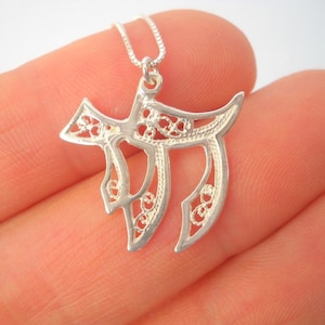 May include: A silver pendant necklace featuring a delicate filigree design of the Hebrew letter Chai, a symbol of life.