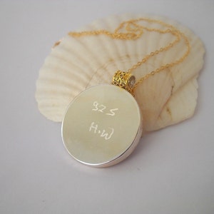 May include: A silver round pendant necklace with a gold chain. The pendant has the inscription "925" and "H-W" on the front.
