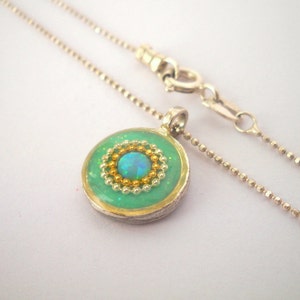 May include: A silver chain necklace with a round pendant featuring a green background, a gold rim, and a blue opal surrounded by gold and green beads.