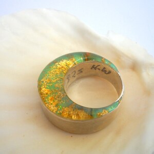 May include: A green and gold ring with a silver band. The ring has a textured surface and is inscribed with the letters "KW" and the number "525".