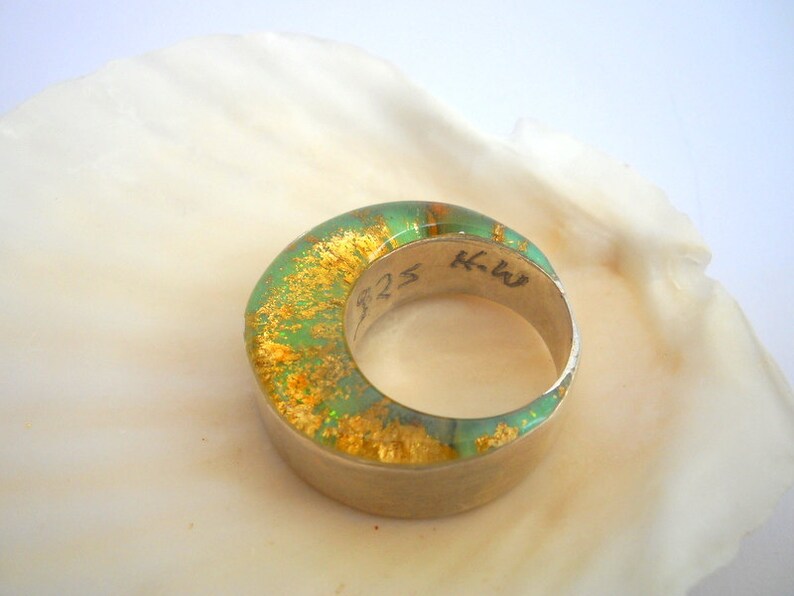 May include: A green and gold ring with a silver band. The ring has a textured surface and is inscribed with the letters "KW" and the number "525".