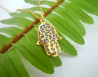 May include: Gold necklace with a blue enamel Hamsa hand pendant. The pendant has intricate filigree details.
