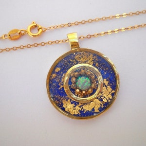 May include: A gold necklace with a round pendant featuring a blue and gold design with a green opal in the center.