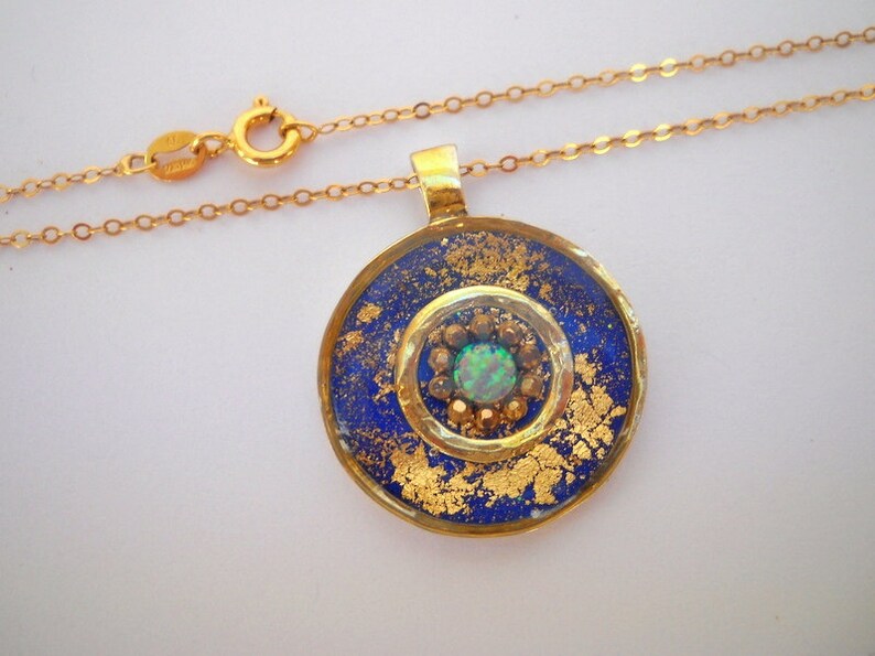 May include: A gold necklace with a round pendant featuring a blue and gold design with a green opal in the center.