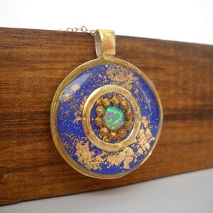 May include: A round pendant necklace with a blue and gold design. The pendant features a green opal gemstone in the center.