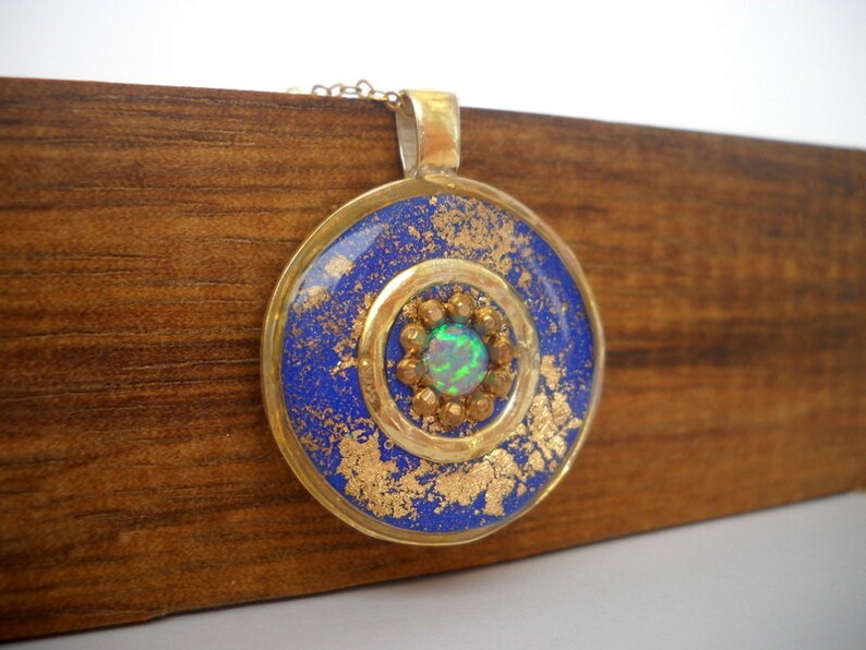May include: A round pendant necklace with a blue and gold design. The pendant features a green opal gemstone in the center.