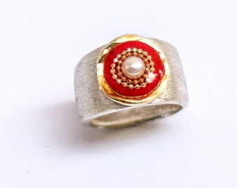 May include: A silver ring with a red enamel center featuring a white pearl surrounded by gold beads.