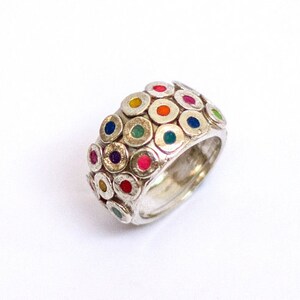 May include: A silver ring with a wide band featuring a pattern of small, raised circles with colorful enamel dots in the center. The ring is a vibrant mix of colors, including red, blue, green, yellow, and purple.