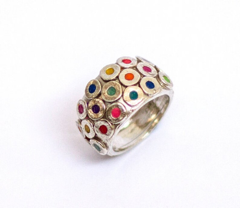 May include: A silver ring with a wide band featuring a pattern of small, raised circles with colorful enamel dots in the center. The ring is a vibrant mix of colors, including red, blue, green, yellow, and purple.