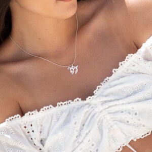 May include: A close-up of a woman wearing a white off-the-shoulder top with delicate lace detailing. She is wearing a silver necklace with a small pendant.